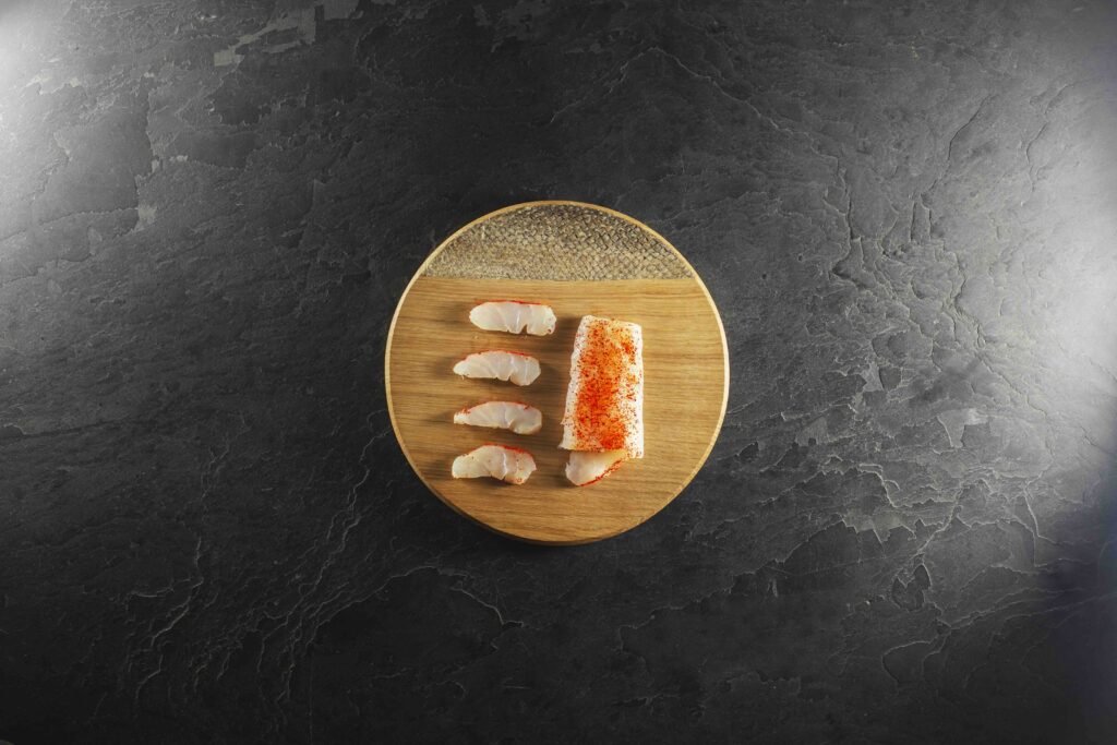 Tranches et pavé de cabillaud fumé saupoudré de piment d'Espelette sur une planche ronde en bois, fond d'ardoise